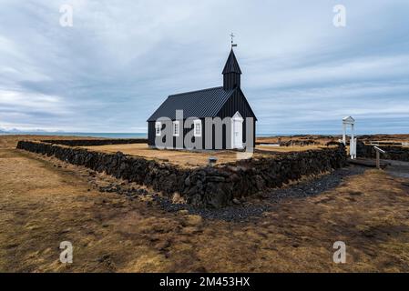 Malerischer Blick auf die späte Winterlandschaft in der berühmten schwarzen Kirche Búðir (oder Budir), umgeben von einer natürlichen Steinmauer, Snæfellsnes, Island Stockfoto