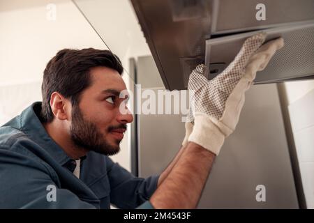 Handwerker in der Uniform, repariert Küchenabsauger, ersetzt Filter in der Dunstabzugshaube. Wartungskonzept Stockfoto