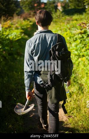 Ein Typ mit Schaufel geht durch Wälder. Ein Mann gräbt Boden. Ein Mann ging in den Wald. Stockfoto