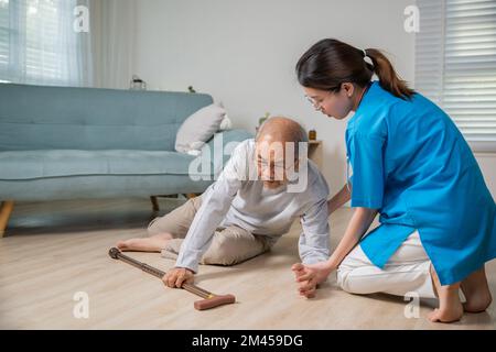 Behinderter alter Mann mit Gehstock fällt auf den Boden und pflegende junge Assistentin Stockfoto