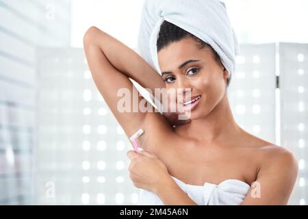 Ich führe Sie durch meine Achselhöhlen. Eine attraktive junge Frau, die sich im Badezimmer mit einem Rasierer die Achselhöhlen rasiert. Stockfoto