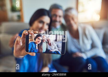 Unsere perfekte Familie. Ein fröhliches Seniorenpaar und ihre Tochter machen zusammen ein Selfie, während sie zu Hause auf einer Couch sitzen. Stockfoto