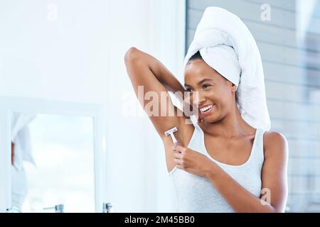 Dein Deodorant wird bei diesen haarigen Achseln nicht wirken. Eine attraktive junge Frau, die sich im Badezimmer mit einem Rasierer die Achselhöhlen rasiert. Stockfoto