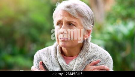 Ich Frage mich, was mein Mann gesagt hätte. Eine sorglose ältere Frau, die auf einer Bank sitzt, während sie im Park im Freien nachdenkt. Stockfoto