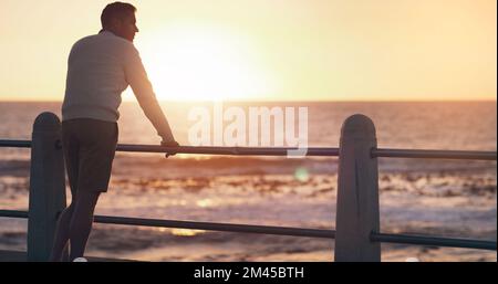 Neue Möglichkeiten liegen vor uns. Rückblick auf einen Mann, der den Sonnenuntergang am Strand beobachtet. Stockfoto