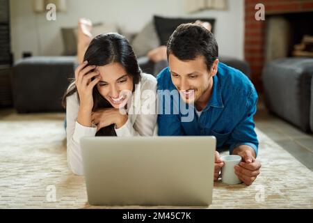 Ich habe ein Wochenende zusammen gebloggt. Ein liebevolles junges Paar, das auf dem Teppich liegt und zu Hause ein digitales Tablet benutzt. Stockfoto