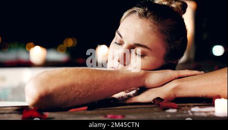Das fühlt sich wie der Himmel auf Erden an. Eine attraktive, reife Frau, die sich nachts mit geschlossenen Augen in einem Whirlpool entspannt. Stockfoto