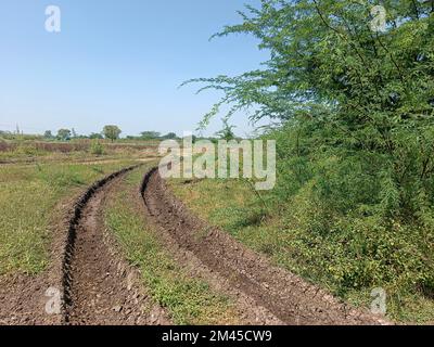 Blick auf die Indian Village Road - Schlammstraße, die mit dem ländlichen Gebiet verbunden ist, auf beiden Seiten Ackerland. Stockfoto