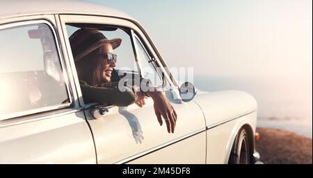 Nichts ist so erfrischend wie eine Fahrt zum Strand. Eine junge Frau, die auf einem Ausflug aus dem Autofenster schaut. Stockfoto