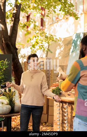 Ein junges, vielfältiges Familienpaar, das sich miteinander unterhält, während es gesundes Bio-Gemüse auf dem Bauernmarkt kauft. Zwei multirassische Freunde, Mann und Frau, die frische lokale Produkte kaufen Stockfoto