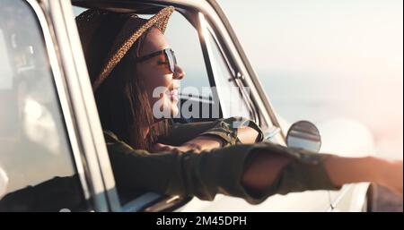 Die frische Luft der Küste zu genießen. Eine attraktive junge Frau, die an einem sonnigen Tag einen Roadtrip genießt. Stockfoto