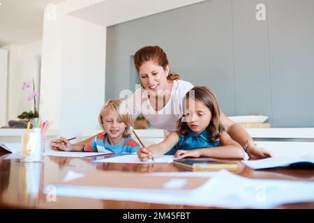 Diese kleinen Köpfe für eine große Zukunft zu Formen. Eine junge Mutter, die ihren beiden kleinen Kindern bei ihren Hausaufgaben zu Hause hilft. Stockfoto