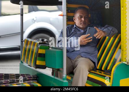 Auto-Fahrer mit Mobiltelefon, während er in der Auto-Rikscha sitzt Stockfoto