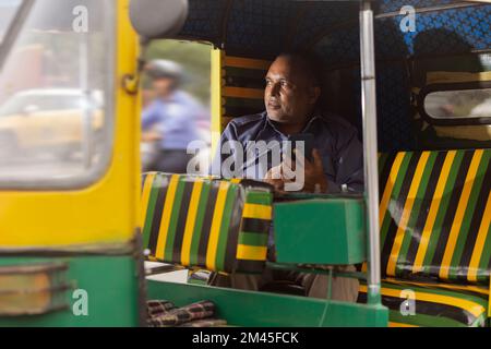 Auto-Fahrer mit Mobiltelefon, während er in der Auto-Rikscha sitzt Stockfoto
