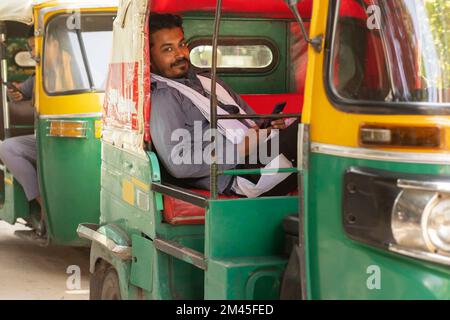 Auto-Rikscha-Fahrer mit Mobiltelefon, während er drinnen sitzt Stockfoto