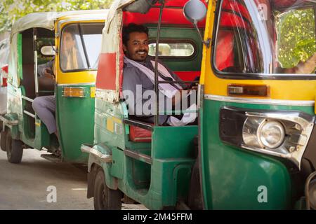 Auto-Rikscha-Fahrer mit Mobiltelefon, während er drinnen sitzt Stockfoto