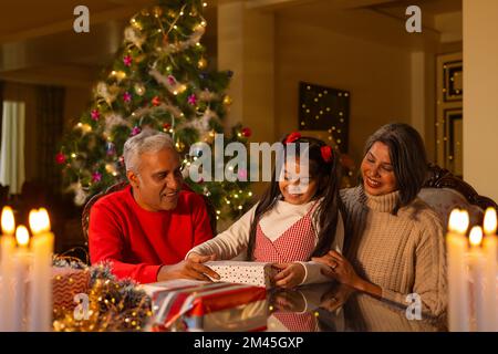 Mädchen öffnet Weihnachtsgeschenk, während sie zu Hause bei ihren Großeltern sitzt Stockfoto