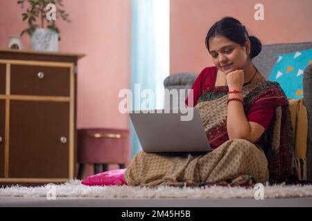 Frau, die auf dem Teppich sitzt und ein Notebook im Wohnzimmer benutzt Stockfoto