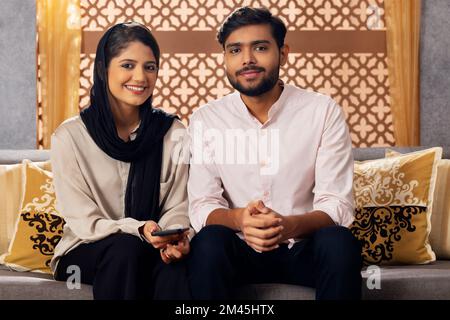 Glückliches muslimisches Paar, das im Wohnzimmer sitzt Stockfoto
