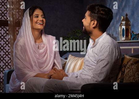 Romantisches muslimisches Paar, das Händchen hält und sich im Wohnzimmer ansieht Stockfoto