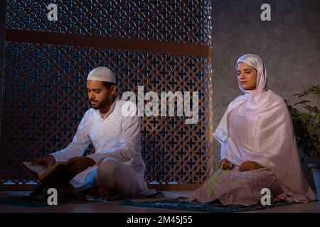 Muslimischer Mann liest Koran und Frau betet mit Gebetsperlen Stockfoto