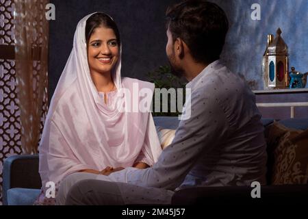Romantisches muslimisches Paar, das Händchen hält und sich im Wohnzimmer ansieht Stockfoto