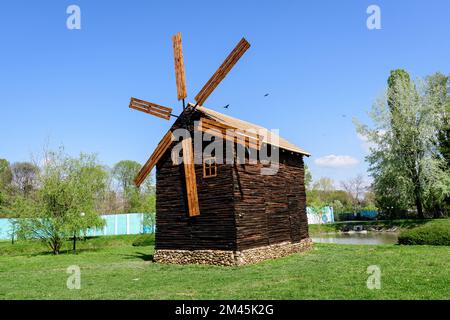 Dekorative alte Holzmühle und grünes Gras auf einer kleinen Insel auf dem See vom Chindiei Park (Parcul Chindiei) in Targoviste, Rumänien, in einem sonnigen SPR Stockfoto