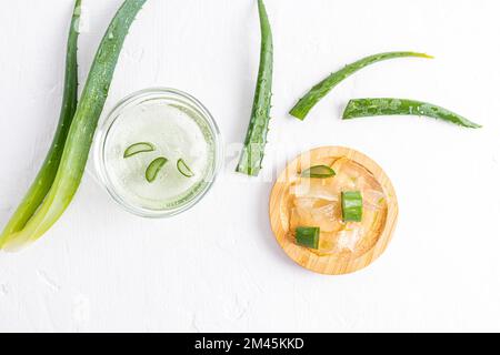 Stücke von durchsichtigem Fruchtfleisch aus Aloe-Vera-Blättern in einer Holzschüssel auf weißem Hintergrund zwischen den saftigen Blättern der Pflanze. Natürliche Hautpflege Stockfoto