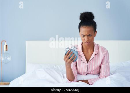 Ich möchte diese Uhr gegen die Wand werfen. Eine attraktive junge Frau, die zu Hause lästig auf ihren Wecker schaut. Stockfoto
