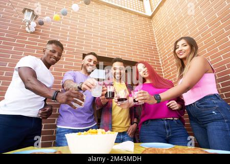 Eine Gruppe von Freunden lächelt, während sie auf einer Party im Freien mit Getränken anstoßen. Freundschaftskonzept. Stockfoto