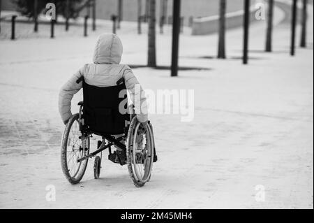 Obdachlose Frau sitzt im Winter im Rollstuhl. Schwarz und weiß. Stockfoto