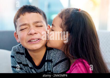 Erst die Nerven küssen. Ein bezauberndes kleines Mädchen küsst zu Hause ihren großen Bruder auf die Wange. Stockfoto