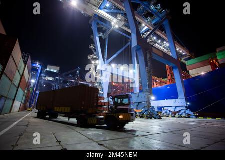 Hafen-Container-Terminal bei Nacht. Bewegungsunschärfe eines Containers auf einem Traktor im Vordergrund. Stockfoto