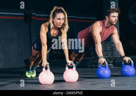 Porträt von zwei Personen, die in einem Fitnessraum mit Kugelhanteln trainieren Stockfoto