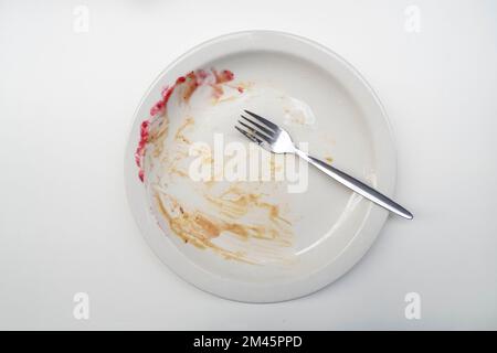 Essensreste mit brauner Sauce, schmutziger Teller und Essensreste, silberne Gabel auf grauem Tisch, Draufsicht Stockfoto