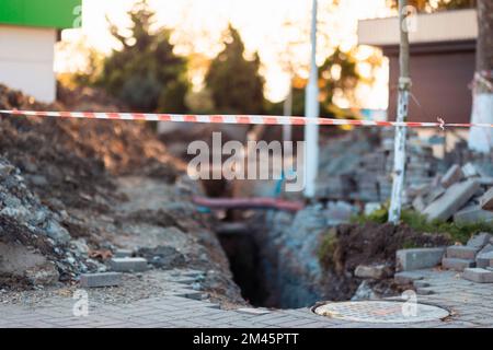 Reparatur der Kanalisation auf der Straße. Ausgegraben, gestapelt Tische und Müll. Bereich der Bauarbeiten Zaun mit Klebeband. Industrielle und städtische Konstrukteure Stockfoto