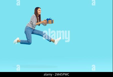 Fröhliche Frau mit Geschenkbox, springt und fliegt auf blauem Hintergrund Stockfoto