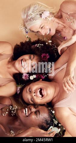 Draufsicht, Vielfalt und Frauen mit Blumen, Kosmetik und Hautpflege auf braunem Studiohintergrund. Multiethnisch, weiblich und weiblich mit positiver Körperhaltung Stockfoto