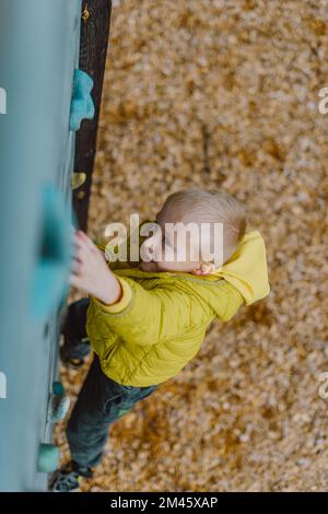 Junge an der Kletterwand ohne Helm, Gefahr an der Kletterwand. Kleiner Junge klettert Eine Felswand in der Halle Stockfoto