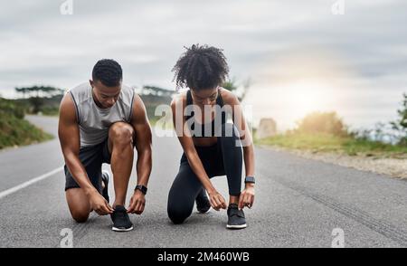 Schnür dich an und lass das Rennen beginnen. Ein sportliches junges Paar, das sich beim Sport im Freien die Schnürsenkel bindet. Stockfoto