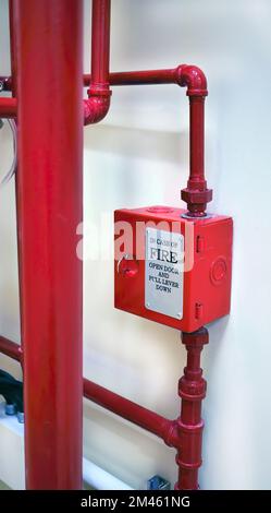 Roter Metallkasten und vertikale Installation roter Rohrleitung der Brandbekämpfungsanlage mit Betonwänden im Gebäude Stockfoto