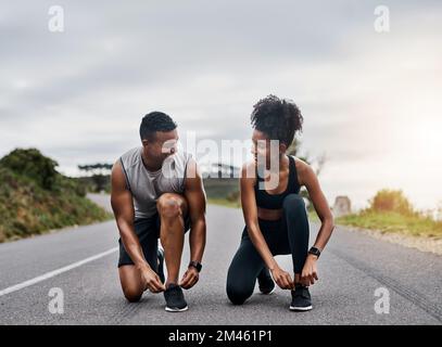 Ich Wette, ich Gewinne dich in einem Rennen. Ein sportliches junges Paar, das sich beim Sport im Freien die Schnürsenkel bindet. Stockfoto