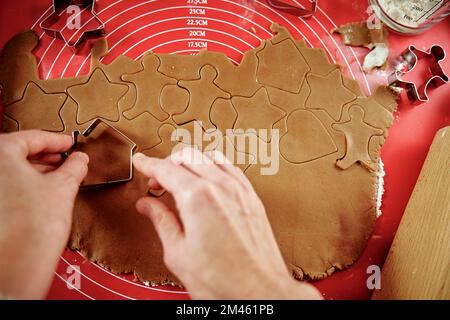 Eine Frau, die Lebkekse in der Küche zubereitet. Weibliche Hände schneiden Ingwerteig mit Schneidewerkzeug, um Kekse für Winterferien zu backen Stockfoto