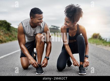 Ich bin bereit, wenn du es bist. Ein sportliches junges Paar, das sich beim Sport im Freien die Schnürsenkel bindet. Stockfoto