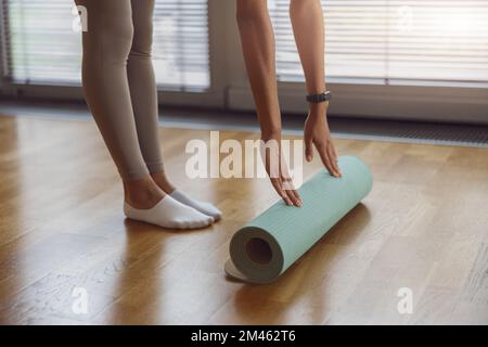 Nahaufnahme einer jungen Frau, die ihre Matte nach dem Yoga-Kurs auf dem Holzboden rollt Stockfoto