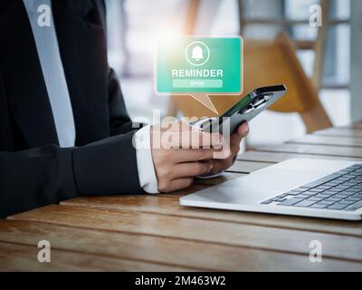 Erinnerungsbenachrichtigung mit Glockensymbol Popup-Meldung auf dem Smartphone-Bildschirm in den Händen eines Geschäftsmanns während der Arbeit mit einem Laptop Stockfoto