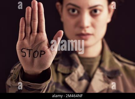 Stopp, Krieg und Hand einer Militärfrau, wütend, frustriert und mit einem Schild vor dunklem, schwarzem Studiohintergrund. Armee, Wut und Porträt eines Soldaten Stockfoto