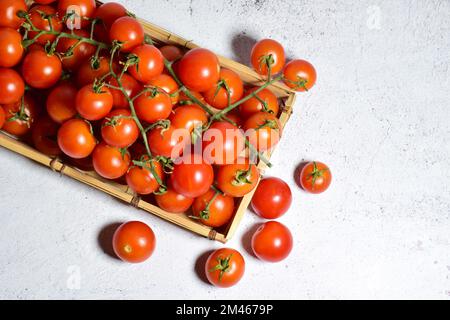 Eine Draufsicht von saftigen Kirschtomaten auf einer Holzschale auf einer Steinoberfläche Stockfoto