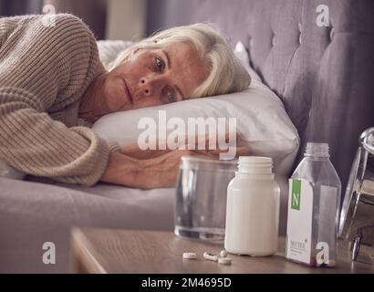 Ältere Frau, Bett und medizinische sucht mit Pillen, Medikamenten oder Medikamenten, während sie zu Hause wach liegen. Ältere Frau, die krank, krank oder Stockfoto