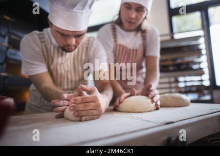 Ein Mann mit daunensyndrom, der mit seinem Kollegen Brot in der Bäckerei vorbereitete. Konzept der Integration von Menschen mit Behinderungen in die Gesellschaft. Stockfoto